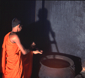 A Young Buddhist monk works in a timeless shadow, stirring a vat of Ayuvedic oil
